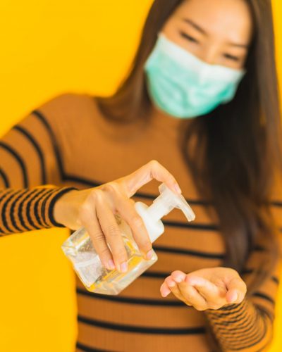 Portrait beautiful young asian woman with mask alcohol spray and gel bottle in her hand for protect from coronavirus or covid19 on yellow isolated background
